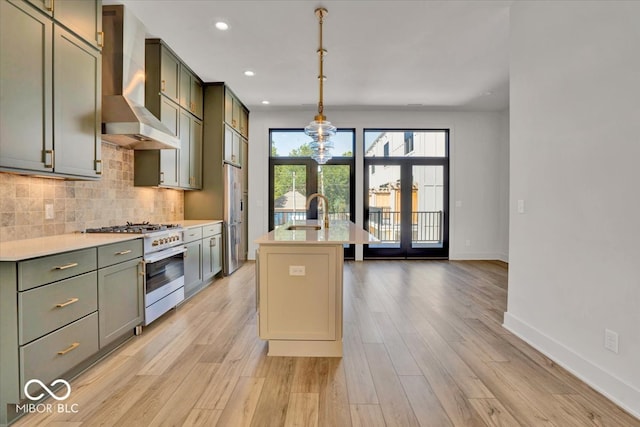 kitchen featuring light hardwood / wood-style flooring, appliances with stainless steel finishes, sink, wall chimney exhaust hood, and a kitchen island with sink