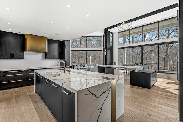 kitchen featuring light stone counters, floor to ceiling windows, sink, light hardwood / wood-style flooring, and a center island with sink