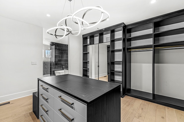 spacious closet featuring a notable chandelier and light hardwood / wood-style flooring