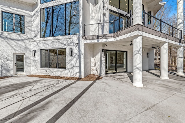 view of exterior entry featuring a balcony, ceiling fan, and a patio