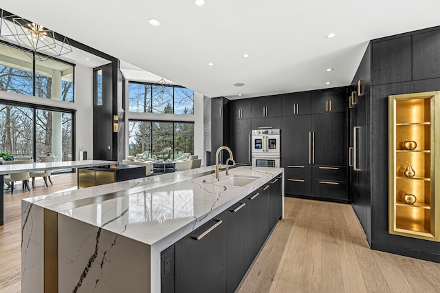 kitchen with an island with sink, light stone countertops, light hardwood / wood-style floors, and sink