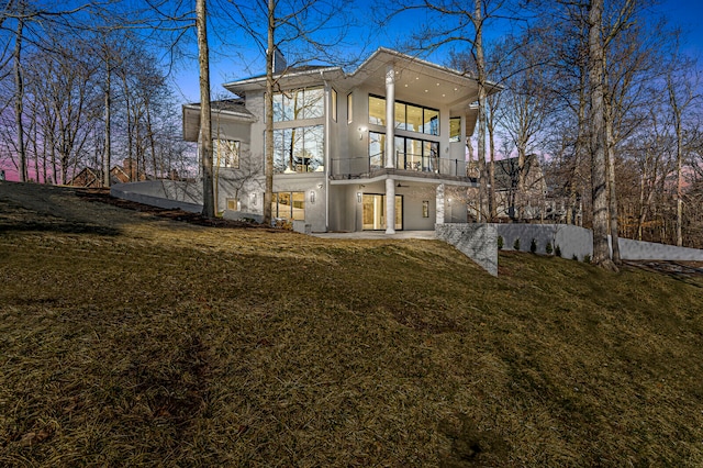 back house at dusk with a balcony and a yard