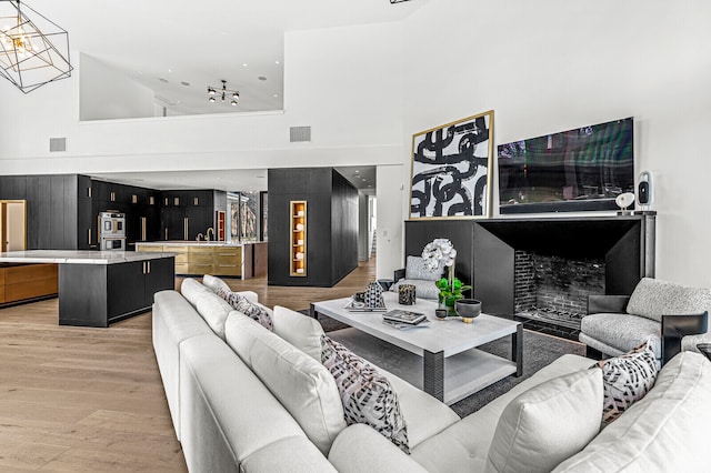 living room featuring light hardwood / wood-style floors, sink, a chandelier, and a towering ceiling