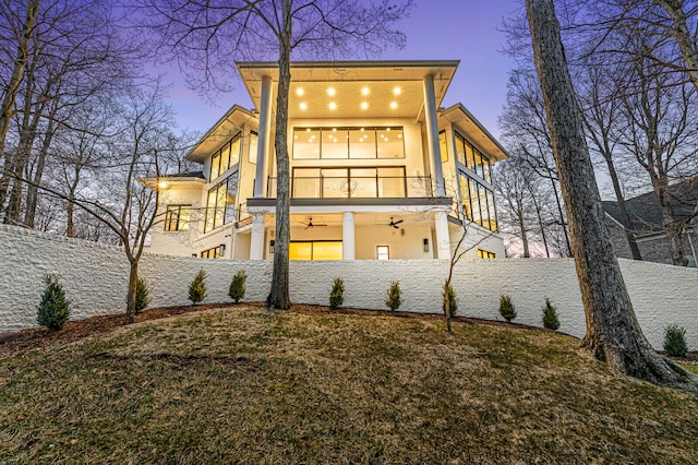 back house at dusk featuring ceiling fan, a lawn, and a balcony