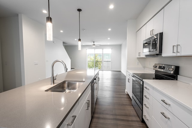 kitchen with dark wood-type flooring, appliances with stainless steel finishes, white cabinets, ceiling fan, and sink