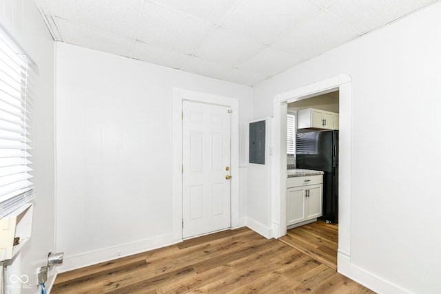 unfurnished room with a paneled ceiling, electric panel, and light wood-type flooring