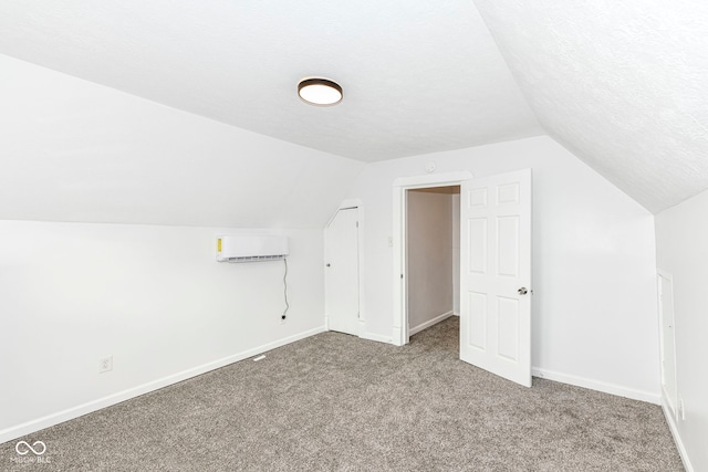 additional living space with lofted ceiling, a wall mounted air conditioner, carpet, and a textured ceiling