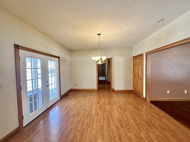 empty room with french doors, a notable chandelier, and hardwood / wood-style flooring