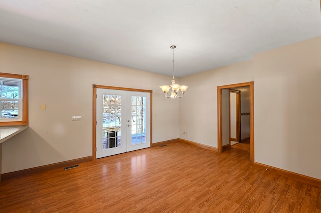 unfurnished room with a notable chandelier, light hardwood / wood-style floors, a healthy amount of sunlight, and french doors