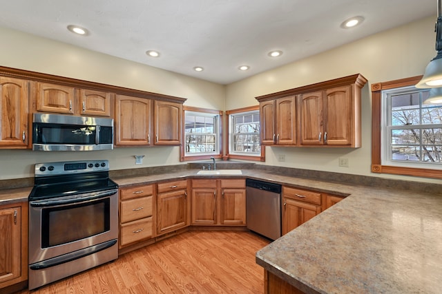 kitchen with light hardwood / wood-style floors, appliances with stainless steel finishes, hanging light fixtures, and sink