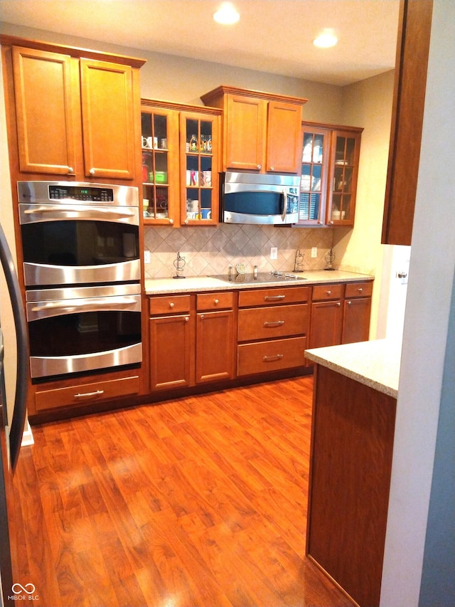 kitchen featuring light stone counters, backsplash, stainless steel appliances, and light hardwood / wood-style floors