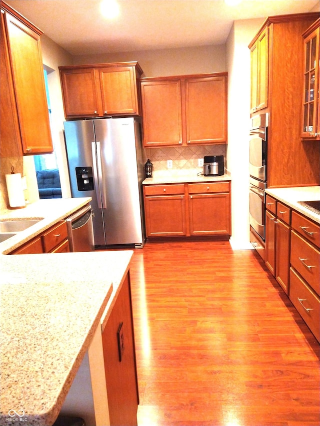 kitchen featuring appliances with stainless steel finishes, tasteful backsplash, sink, light stone counters, and light hardwood / wood-style flooring