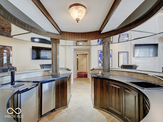 kitchen with dark brown cabinetry, sink, tasteful backsplash, refrigerator, and decorative columns