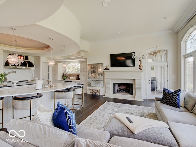 living room featuring sink, crown molding, dark wood-type flooring, a notable chandelier, and a tray ceiling