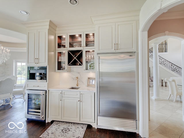 bar with sink, black oven, wine cooler, white cabinets, and built in fridge