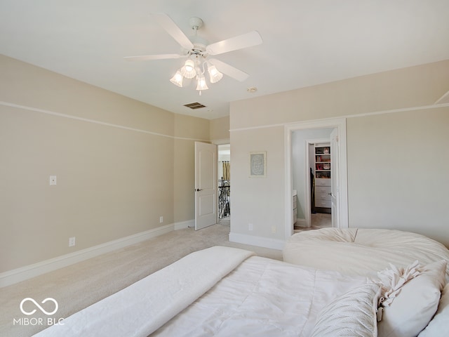 bedroom with ceiling fan, light colored carpet, and a walk in closet