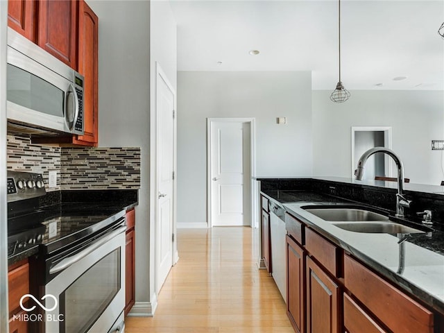 kitchen with hanging light fixtures, dark stone counters, stainless steel appliances, sink, and light hardwood / wood-style flooring