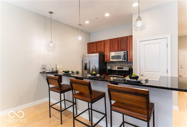 kitchen with a breakfast bar, light hardwood / wood-style floors, appliances with stainless steel finishes, and pendant lighting