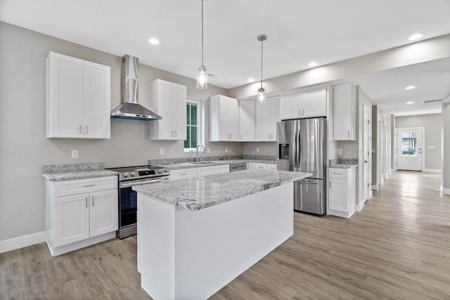 kitchen with white cabinets, stainless steel appliances, light wood-type flooring, pendant lighting, and wall chimney range hood