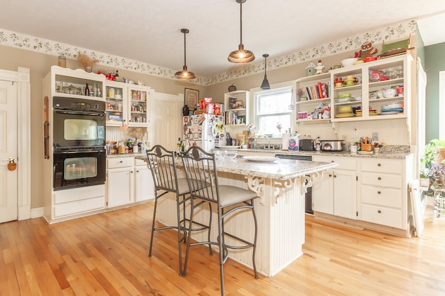 kitchen featuring hanging light fixtures, a kitchen island, double oven, white fridge, and light wood-type flooring