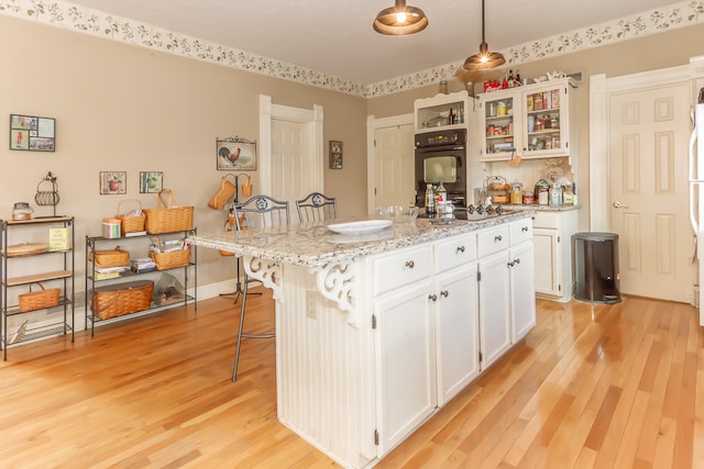 kitchen with black appliances, a kitchen island, hanging light fixtures, a breakfast bar, and white cabinets