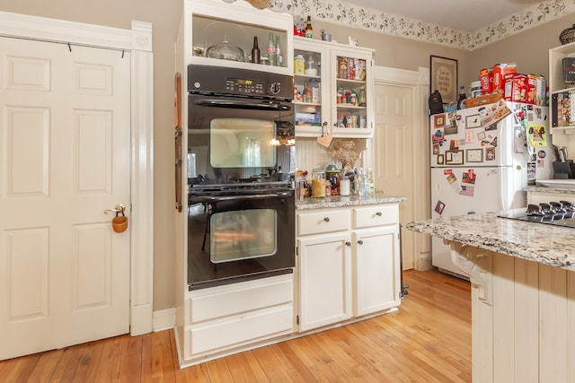 kitchen with white fridge, light stone countertops, white cabinets, black double oven, and light wood-type flooring