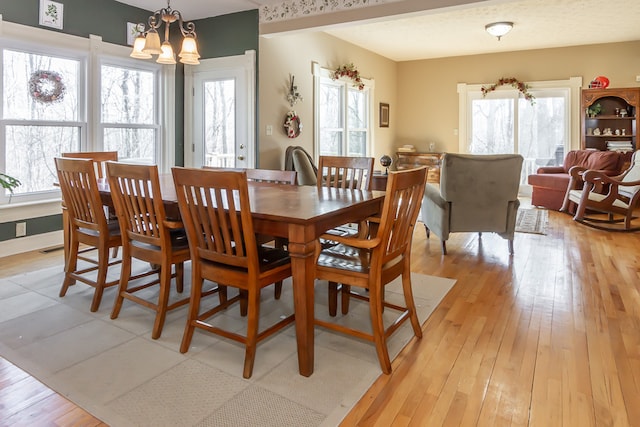 dining space with light hardwood / wood-style floors, a healthy amount of sunlight, and a notable chandelier