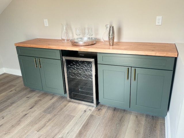 bar featuring green cabinets, wine cooler, light hardwood / wood-style floors, and butcher block counters