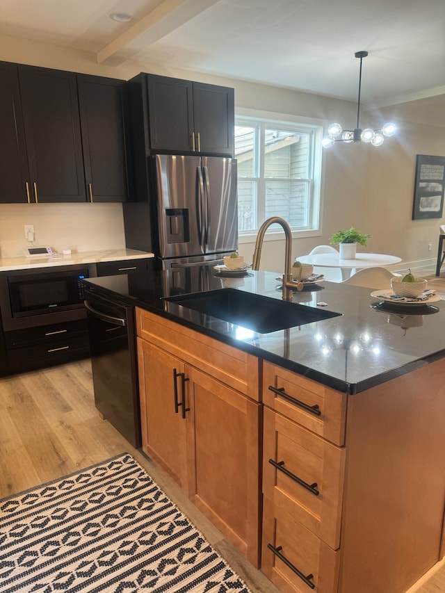 kitchen featuring dark stone countertops, light hardwood / wood-style floors, black appliances, hanging light fixtures, and sink