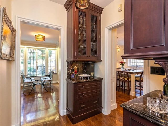 kitchen with dark stone countertops, crown molding, backsplash, and dark hardwood / wood-style flooring