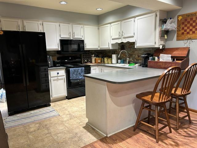 kitchen with black appliances, kitchen peninsula, sink, and white cabinets