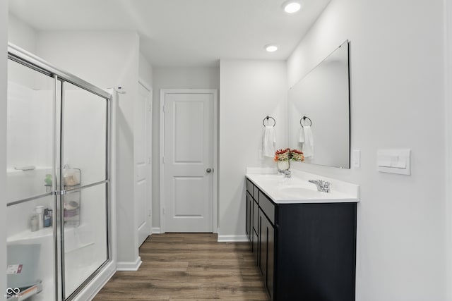 full bathroom with wood finished floors, a shower stall, recessed lighting, double vanity, and baseboards