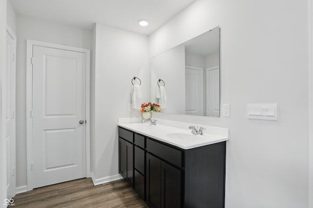 bathroom featuring wood finished floors, double vanity, baseboards, and recessed lighting