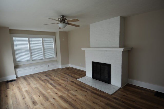 unfurnished living room featuring ceiling fan, brick wall, a brick fireplace, and wood-type flooring