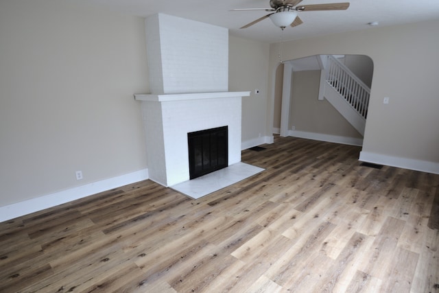 unfurnished living room with a brick fireplace, brick wall, ceiling fan, and light hardwood / wood-style flooring