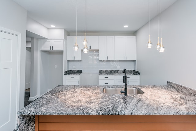 kitchen with sink, light stone counters, decorative light fixtures, decorative backsplash, and white cabinets