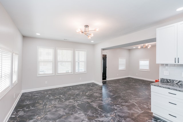 interior space with stone counters, a notable chandelier, a healthy amount of sunlight, and white cabinets