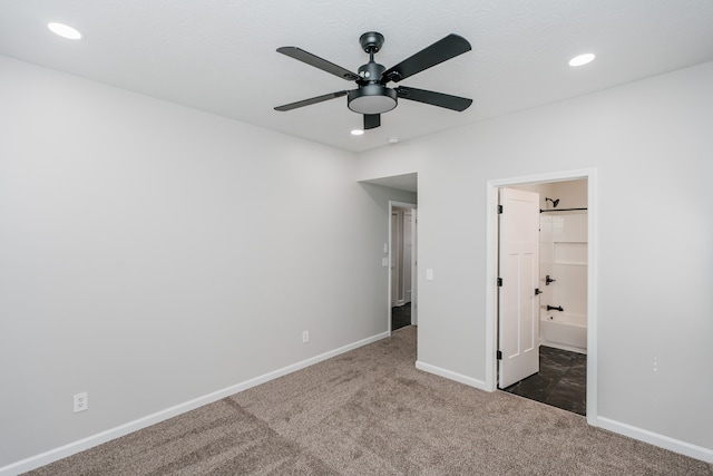 unfurnished bedroom with ceiling fan, ensuite bathroom, and dark carpet