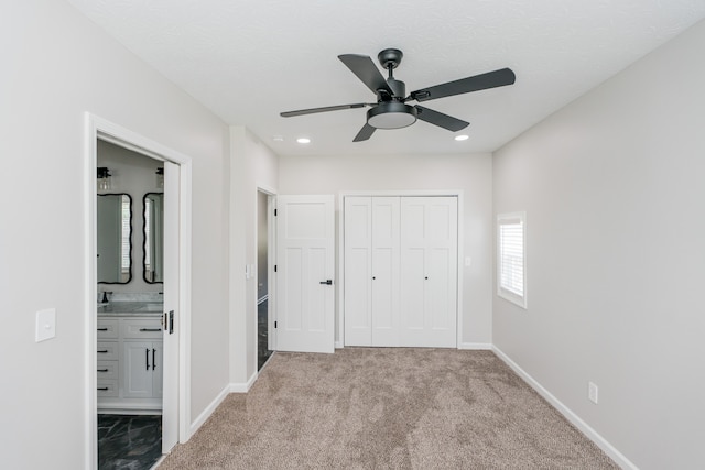 unfurnished bedroom with sink, ensuite bath, light colored carpet, a closet, and ceiling fan