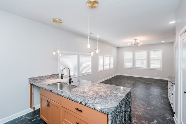 kitchen featuring hanging light fixtures, light stone countertops, sink, and a kitchen island with sink