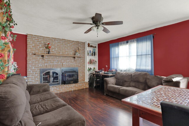 living room with a brick fireplace, ceiling fan, built in shelves, dark hardwood / wood-style flooring, and a textured ceiling