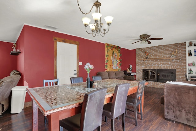 dining area featuring dark hardwood / wood-style flooring, a fireplace, ceiling fan with notable chandelier, and brick wall