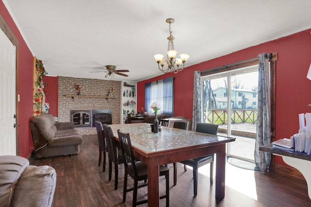 dining space with brick wall, dark hardwood / wood-style floors, a brick fireplace, and ceiling fan with notable chandelier