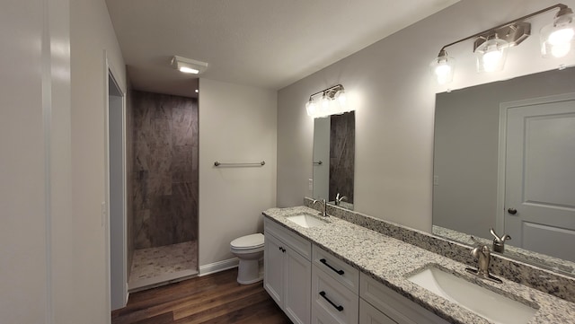 bathroom featuring hardwood / wood-style flooring, toilet, tiled shower, and dual bowl vanity