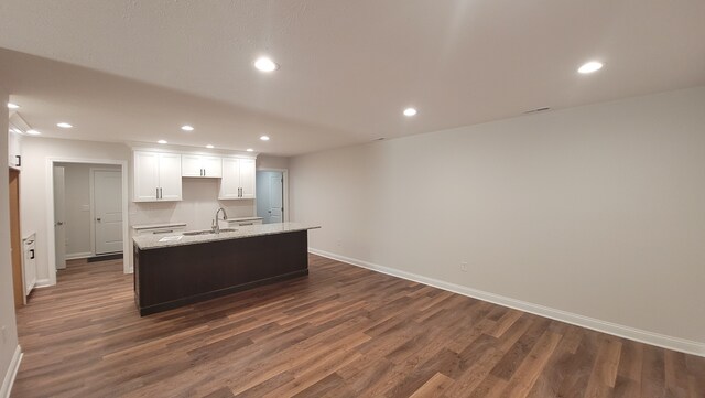 kitchen with light stone counters, white cabinetry, dark hardwood / wood-style floors, a kitchen island with sink, and sink