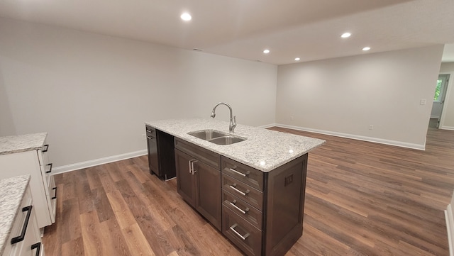 kitchen featuring dishwasher, dark wood-type flooring, sink, light stone counters, and a center island with sink