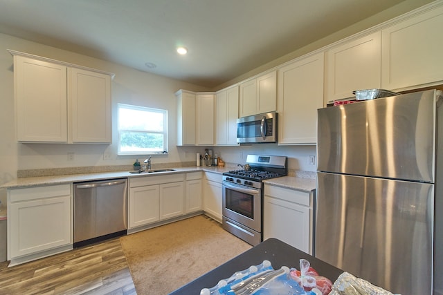 kitchen with appliances with stainless steel finishes, white cabinets, light wood-type flooring, light stone countertops, and sink