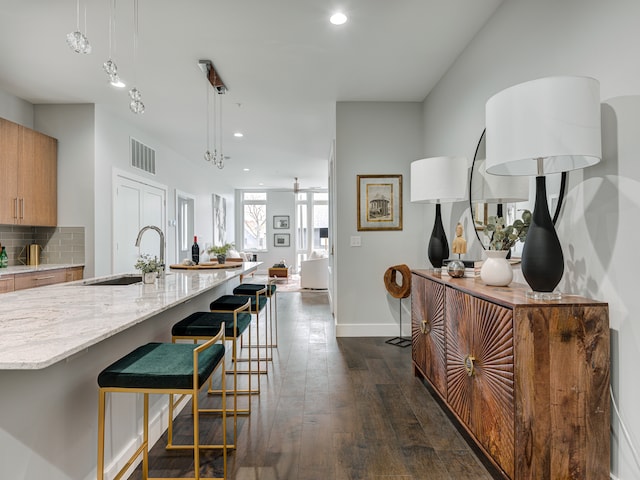 kitchen with a kitchen breakfast bar, light stone countertops, dark wood-type flooring, backsplash, and hanging light fixtures