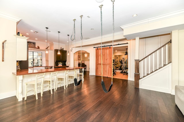 kitchen featuring a barn door, kitchen peninsula, a breakfast bar area, crown molding, and dark hardwood / wood-style flooring