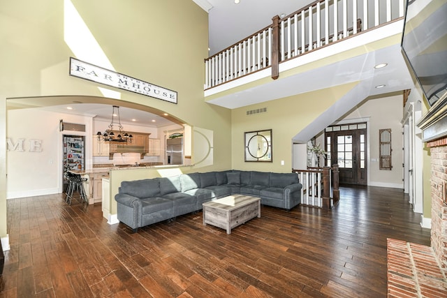 living room with crown molding, an inviting chandelier, dark hardwood / wood-style floors, and a towering ceiling